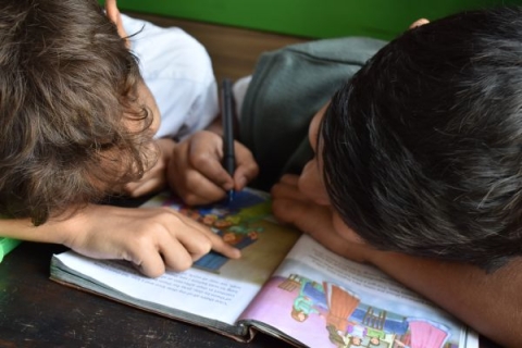 Two boys reading and writing in a book.