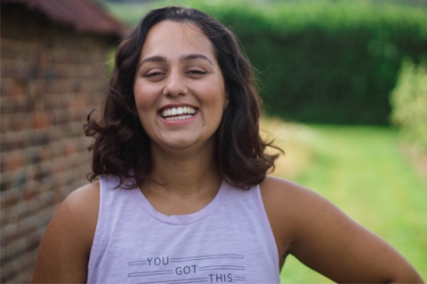 Rosaria Barreto smiling to camera wearing a vest top which says 'YOU GOT THIS'