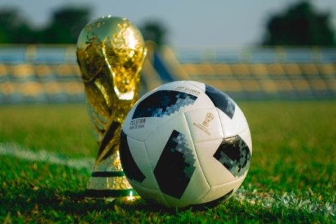 The world cup trophy next to a football on a football pitch