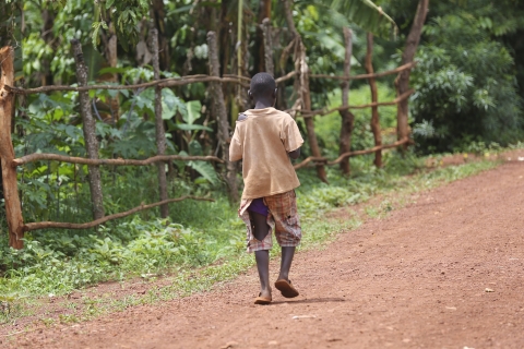 A child wearing no shoes and shorts with a large rip in them walking with his back turned towards the camera