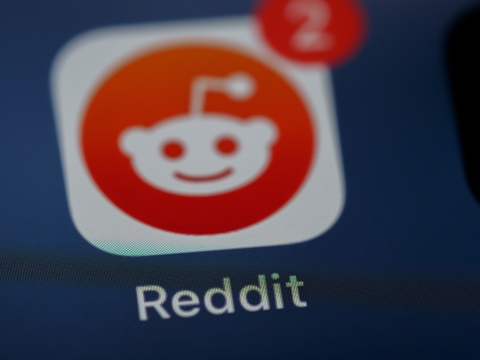 Image shows the Reddit app (a small white alien head on a red background) on a mobile phone screen