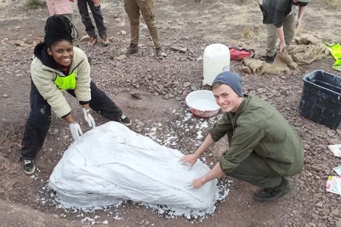 Two people covering dinosaur fossils on ground
