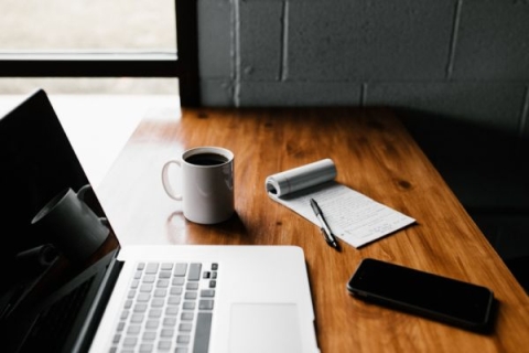 desk with macbook, phone, notepad and coffee on it