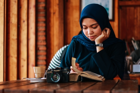 a-young-woman-in-a-head-scarf-sitting-at-a-table-reading-a-book