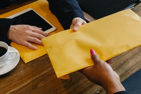 Person with pink nails handing envelope to person in suit