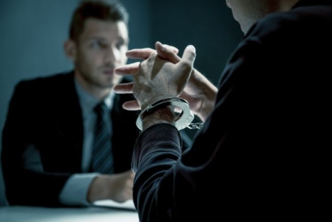 A man in handcuffs talking to a man in a suit