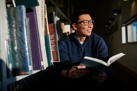 Male student smiling and browsing books in library
