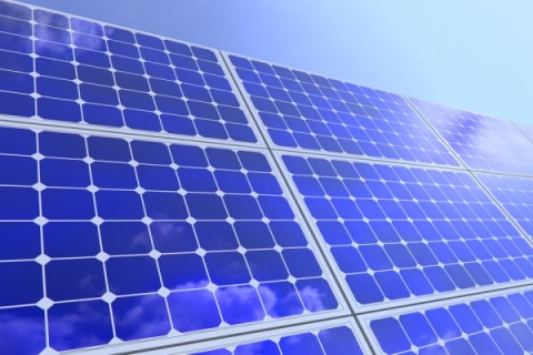 A close-up image of solar panels, which are big black squares against a blue sky