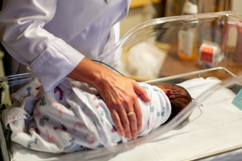 Person in white scrubs holding hand over baby in hospital