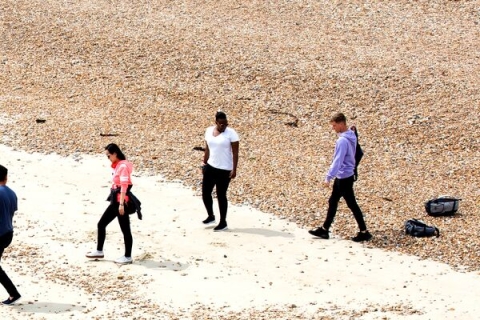Four students walking along southsea beach picking up plastic waste