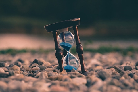 A wooden hourglass filled with blue sand on rocky ground
