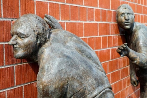Sculptures of two people with ears pressed against a brick wall