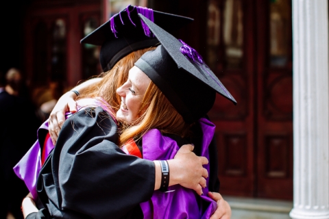 Two graduates hugging in their robes 