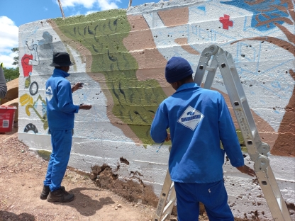 Two people in blue jumpsuits painting a mural