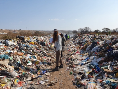 Research Associate Stephanie Northen stood facing the camera with piles of discarded waste surrounding her