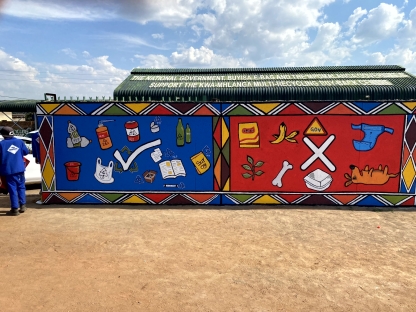 The finished mural. On the left side of the wall are paintings of items that can be recycled, shown clearly by a tick in the middle. On the right are items that cannot be recycled, shown with a large cross in the middle. The mural uses a variety of bright colours and is extremely eye catching. 
