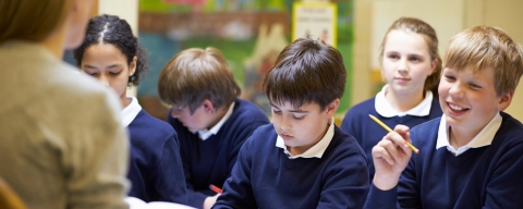 School children in a classroom, sitting at a desk with workbooks