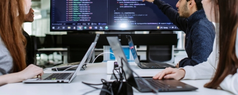 Students discussing the coding that is displayed on the large TV screen in front of them 