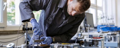 Student in overalls adjusting vice grip under supervision of staff member at Technology Facilities