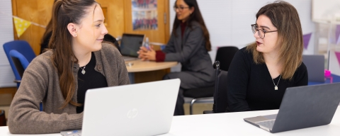 Two women using laptops and talking 