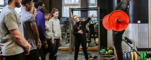  A group of students watching someone demonstrate lifting weights