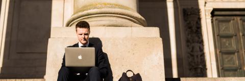 Journalist on guildhall steps writing story on laptop