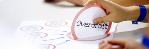 A hand holding an 'Overdraft' popup sign from a diagram on a desk