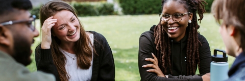 Students smiling in sun at picnic table outside of the Students' Union