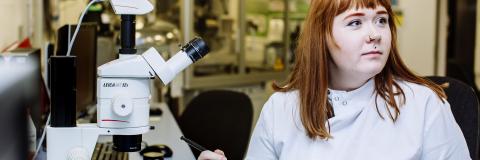 A female student in a lab coat with a microscope