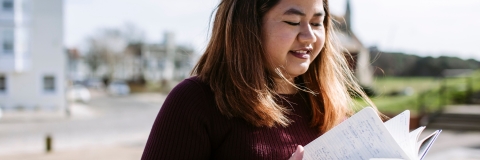 Headshot of postgraduate student smiling, reading a notebook outside
