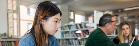 Female student with long hair in the library on a computer