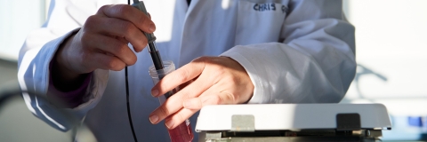 A female student next to window in science lab wearing a white lab coat and a purple scarf