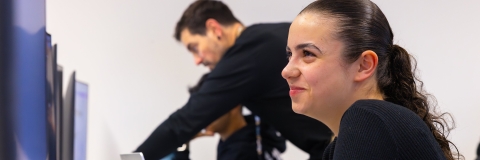 student smiling using computer with lecturer assisting the person next to them