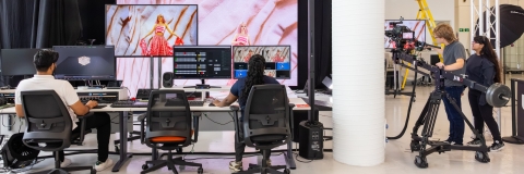 students working on computers with a smart stage in the background with a student in a pink dress modelling a garment