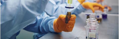 Person in biomedical overalls and yellow gloves extracting a solution from vials