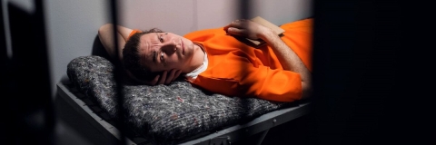 A prisoner in a cell in an orange jumpsuit
