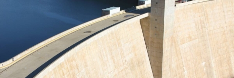 A huge sandy-coloured concrete dam holds back a body of blue water