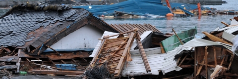 Mostly wooden debris from a tsunami piled up next to a damaged building