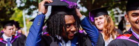 Male student with dreadlocks in graduation robes and hat