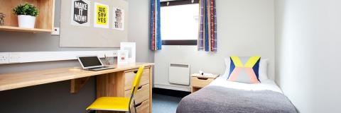 A bedroom in student halls with a bed, desk, and chair