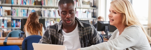 A teacher with a student, both looking at a laptop