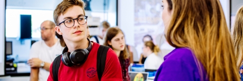 A male with glasses and headphones talking to a student ambassador