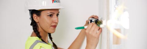 A woman in hard hat and viz jacket measuring a wall