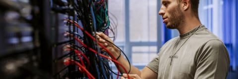Student adjusts ethernet connections at a server board in Technology Facilities