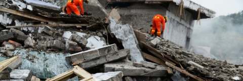 two people in high visibility suits searching through a pile of rubble and debri