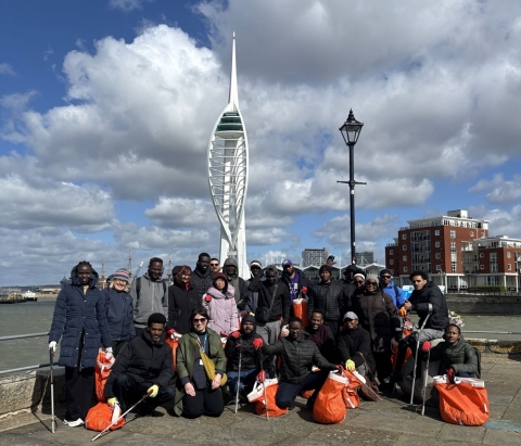 Group posing with collected rubbish bags by waterfront, with landmark tower behind.