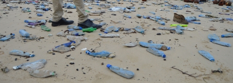 A man stands at a beach front polluted with plastic bottles in Likoni, Mombasa.