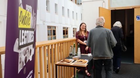 University staff welcoming two members of the public to the lecture