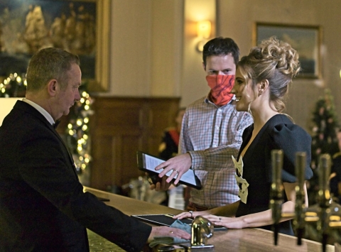 Waiter serving woman at bar while man in mask looks on.