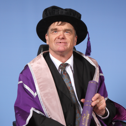 Kevin Holmes holding scroll in graduation gown and cap smiling to camera